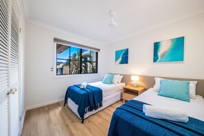 A hotel room with two beds, a window with a view of palm trees, and artwork on the walls. - Blue Beyond Airlie (Airlie Beach)