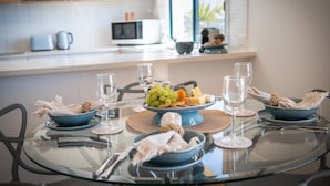 Cocina moderna con una mesa de comedor lista para una comida, mostrando un cuenco de fruta, copas de vino y servilletas dobladas con cuidado.