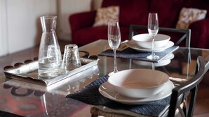 A dining table set with clear glassware, plates, and a pitcher, with a red sofa in the background.