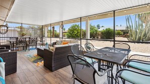 An outdoor patio area with wicker furniture, a dining table, and a view of desert vegetation. - 55+ Comfort & Quiet | 2BR Peaceful Home (Sun City West)