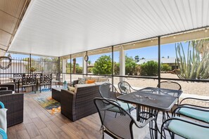 An outdoor patio area with wicker furniture, a dining table, and a view of desert vegetation. - 55+ Comfort & Quiet | 2BR Peaceful Home (Sun City West)