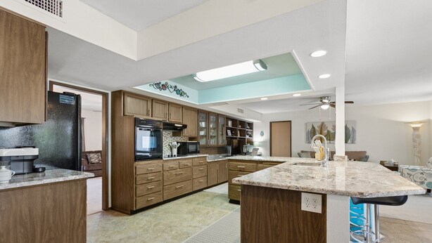 A modern kitchen with wooden cabinets, granite countertops, and a central island with bar stools. - 55+ Comfort & Quiet | 2BR Peaceful Home (Sun City West)