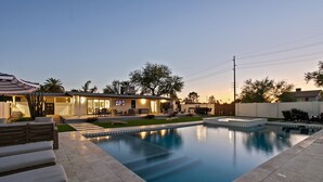 Un área de piscina exterior moderna con una piscina cristalina, sillas de descanso y un patio con televisor.