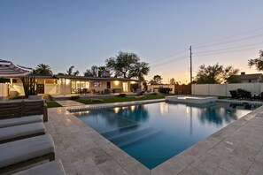 A modern outdoor pool area with a clear pool, lounge chairs, and a patio with a TV. - Camelback Casa | 4BR | Heated & Cooled Pool (Scottsdale)