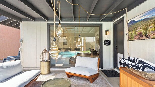 An outdoor seating area with a pool, a white cushioned chair, hanging light fixtures, and a wooden bench with a patterned rug. - 3BR w/ FREE Pool Heat | Hatcher Hideaway (Glendale)