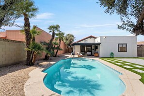 A swimming pool with a tiled deck, surrounded by palm trees and a small patio area with outdoor furniture. - 3BR w/ FREE Pool Heat | Hatcher Hideaway (Glendale)