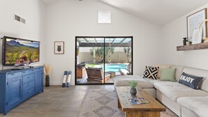 A living room with a TV, sofa, coffee table, and a view of a backyard with a pool. - 3BR w/ FREE Pool Heat | Hatcher Hideaway (Glendale)