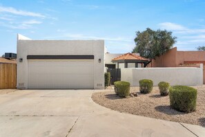 A modern house with a white garage door, a small garden with trimmed bushes, and a tree in the background. - 3BR w/ FREE Pool Heat | Hatcher Hideaway (Glendale)