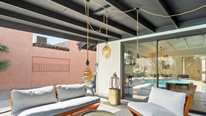 A modern outdoor seating area with two sofas and a table, a glass door leading to a pool, and a hanging light fixture. - 3BR w/ FREE Pool Heat | Hatcher Hideaway (Glendale)