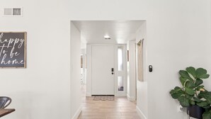 A hallway with a wooden floor, a black and white sign on the left, and a potted plant on the right. - 3BR w/ FREE Pool Heat | Hatcher Hideaway (Glendale)