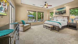A bedroom with a large bed, a ceiling fan, and a view of the outdoors through large windows. - Desert Haven: Pool, SPA, Mini-Golf, and More (Indio)