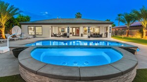 A modern house with a swimming pool, outdoor furniture, and a well-lit patio area. - Desert Haven: Pool, SPA, Mini-Golf, and More (Indio)