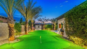A well-maintained golf course with a putting green, palm trees, and a stone wall in the background. - Desert Haven: Pool, SPA, Mini-Golf, and More (Indio)