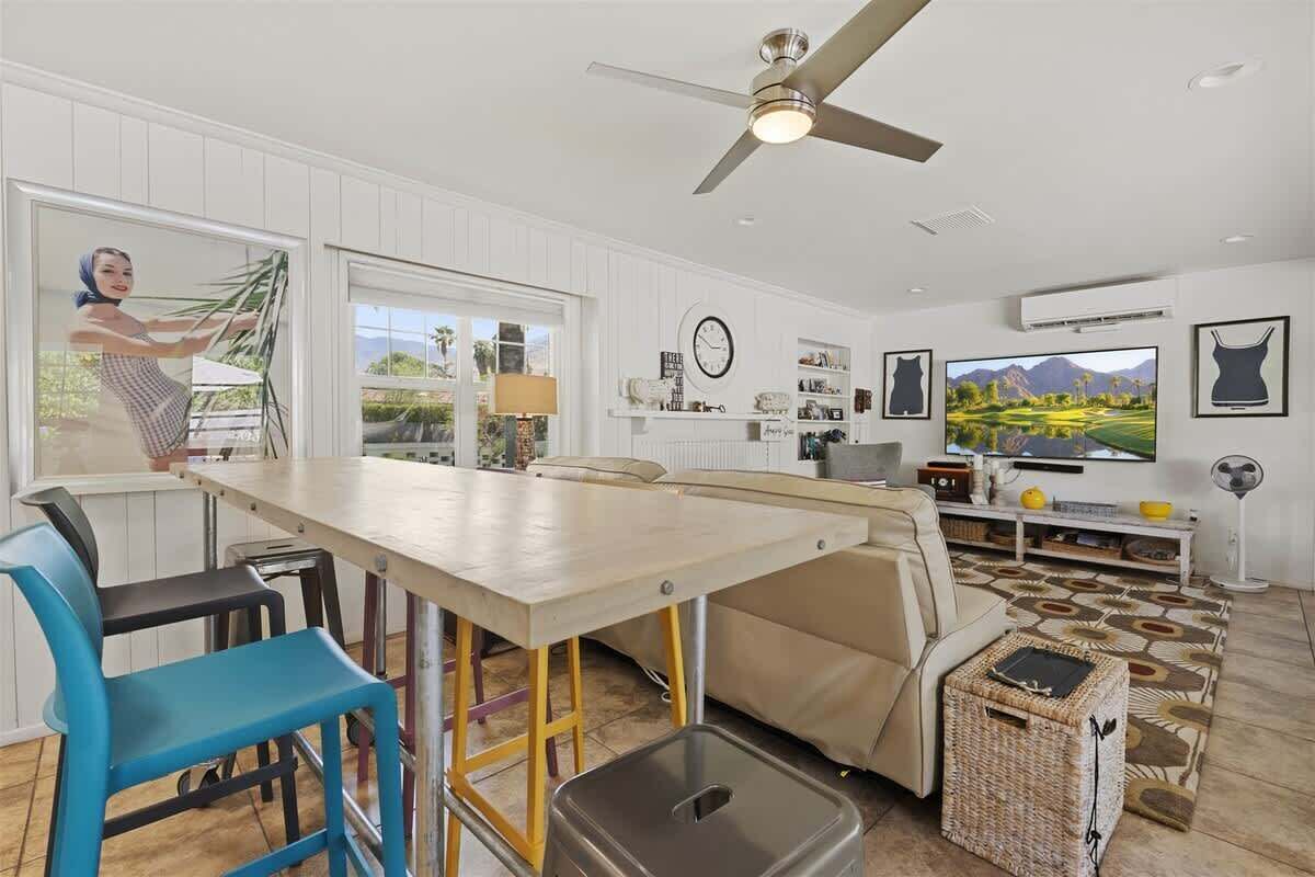 A modern kitchen with a dining table, bar stools, a ceiling fan, and a large window.
