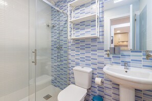 A bathroom with a glass shower enclosure, a toilet, a sink, and a mirror. - Bermeja Village | Balcony & Scenic Street (Marbella)