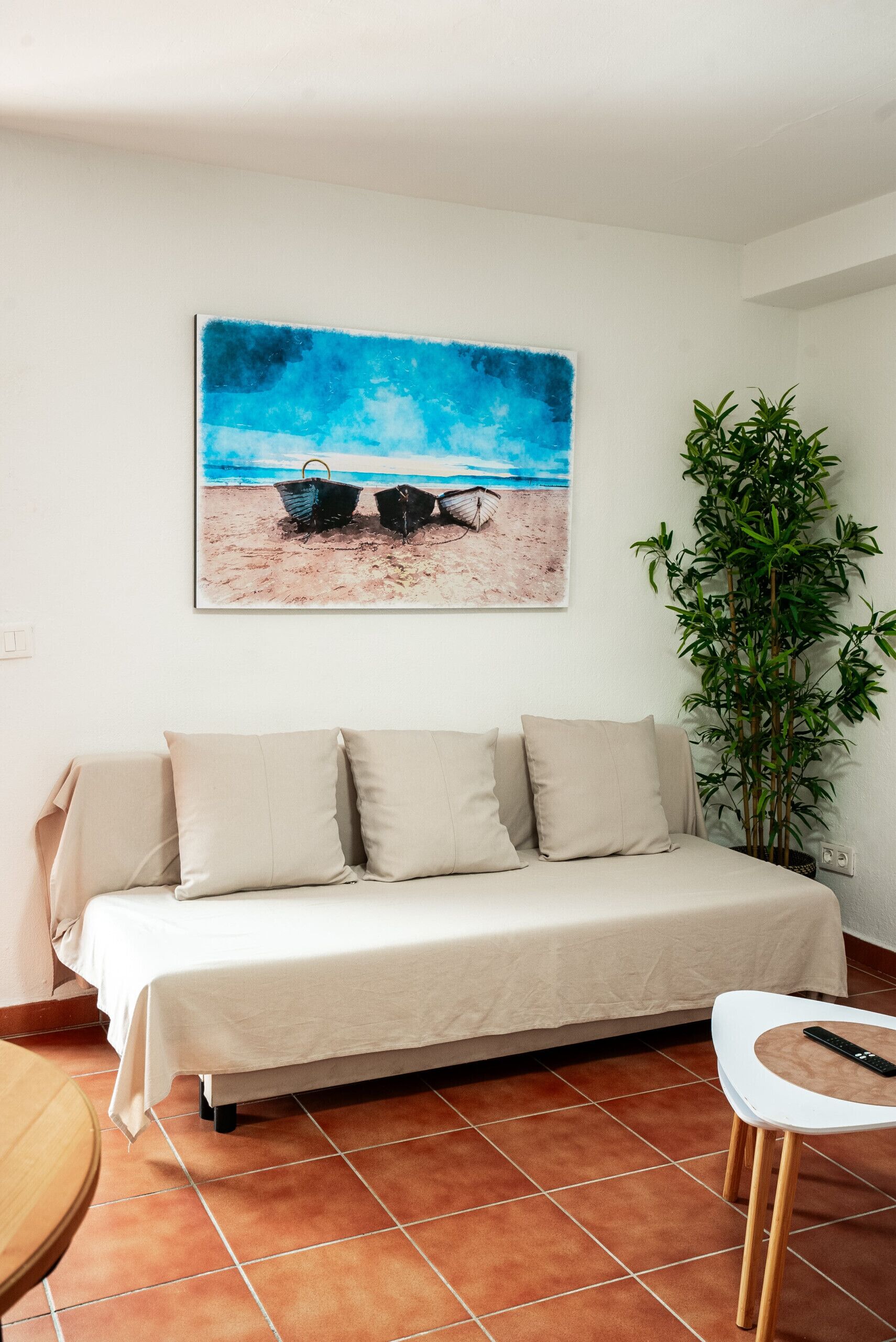 Um quarto com uma cama, uma planta e uma pintura de uma praia.