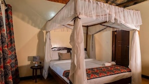 A four-poster canopy bed with a patterned bedspread, a bedside table with a lamp, and a wooden door in the background.