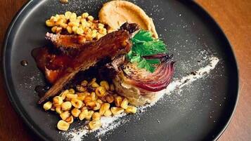 A plate with a dish consisting of meat, corn, and a garnish on a dark plate.
