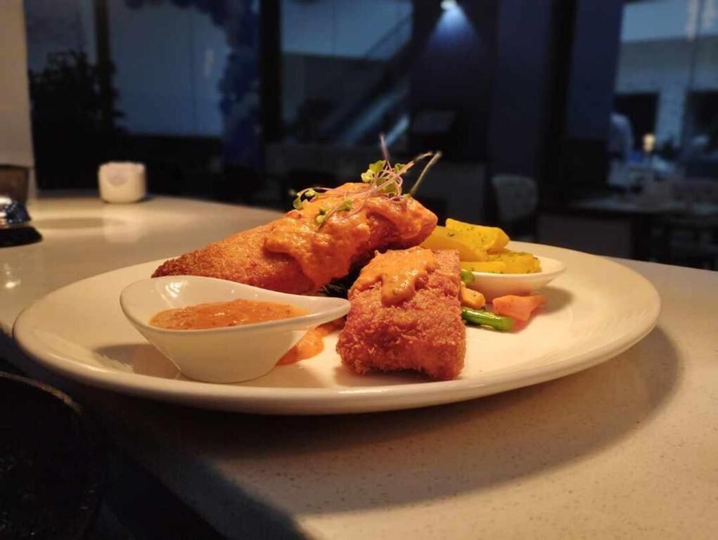 A plate of food with breaded chicken, vegetables, and a side of sauce.