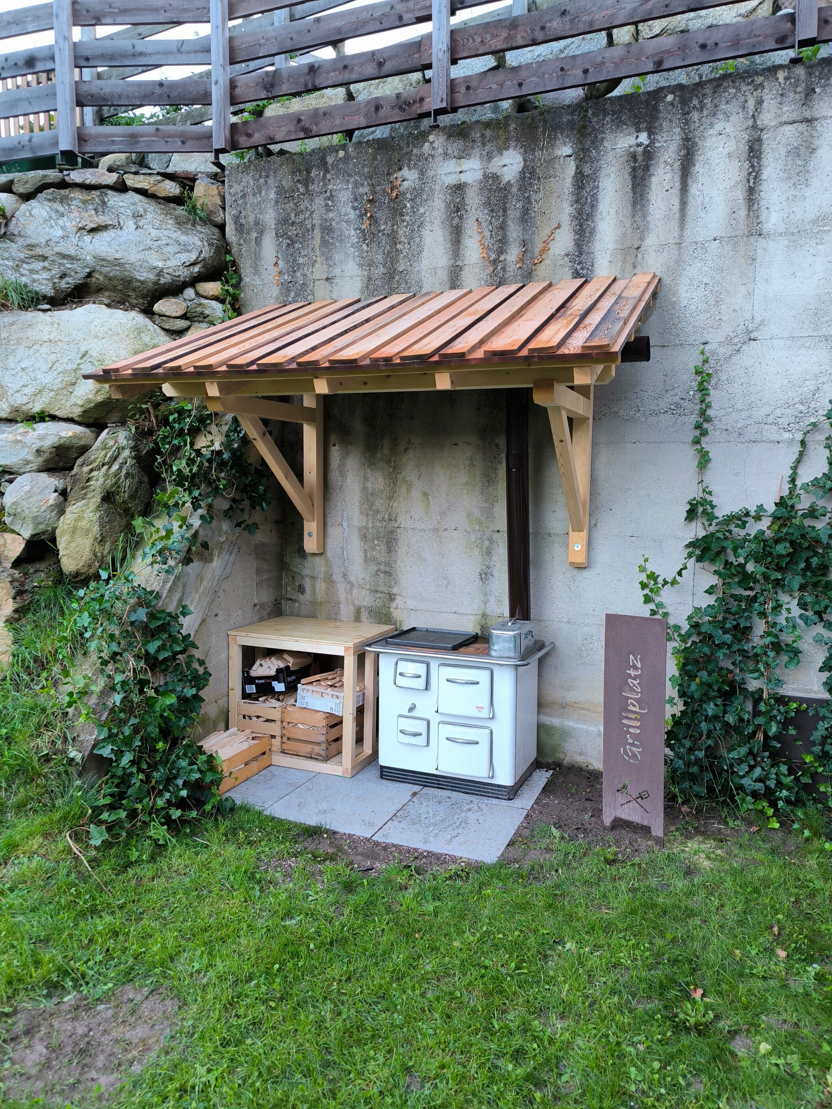 Ein rustikaler Grillbereich im Freien mit einem Holzdach und einem Kühlgerät im Vintage-Stil.