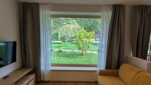 Una habitació amb una finestra gran, un sofà, un televisor sobre un suport de fusta i un petit armari de fusta.
