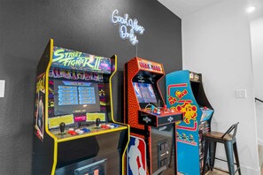 Des bornes d’arcade, dont Street Fighter II et NBA Jam, dans une pièce aux murs sombres, illuminée par un panneau néon.