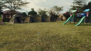 Un campo cubierto de césped con varias tiendas de campaña y un parque infantil con un tobogán.