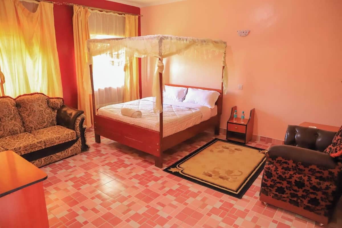 Un dormitorio con cama con dosel, un sofá, una silla y una pequeña mesa con botellas.
