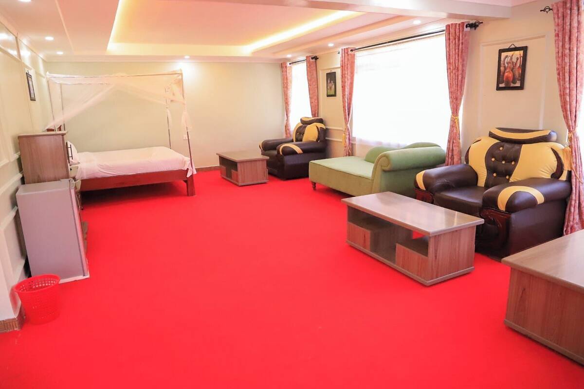Habitación de hotel con cama, sofá, sillón, una mesita y ventana con cortinas.