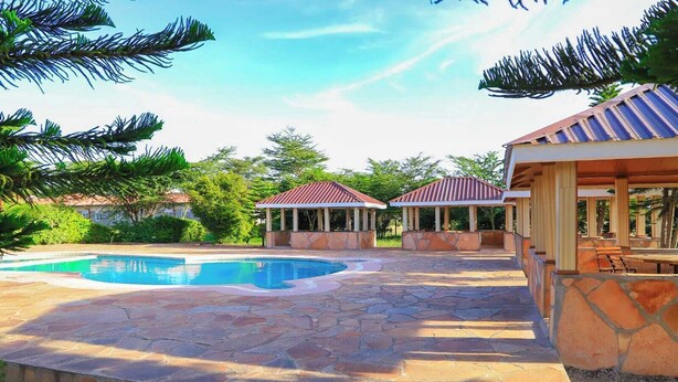 Una piscina con baldosas de piedra, dos gazebos cubiertos y un patio con mesa y sillas.