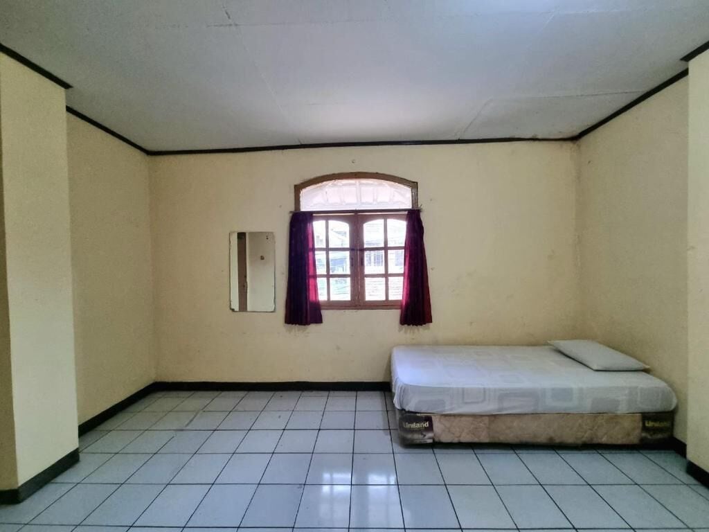 Una habitación pequeña y sencilla con una cama individual, una ventana con cortinas y piso de baldosas.