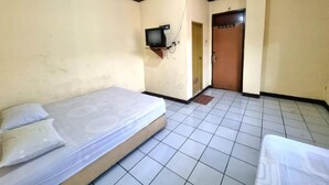 Una habitación pequeña y sencilla con una cama, un televisor colgado en la pared y una puerta que da a otra habitación.