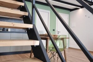 A staircase with wooden steps and black metal railings, leading to a room with a green chair and a table. - Carob Apartments - Life (Trani)