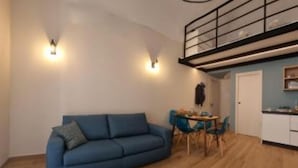 A modern living room with a blue sofa, a dining table with chairs, a staircase, and a kitchen area. - Carob Apartments - Life (Trani)