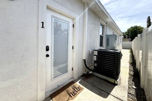 Un immeuble d’habitation avec une porte portant un numéro, un paillasson et un appareil de climatisation installé à l’extérieur.