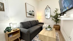 A modern living room with a dark grey sofa, a wooden coffee table, a patterned rug, a small side table with a lamp, and a wall-mounted TV. - Private 1 bedroom luxury mother-in-law suite close proximity to Midtown Tampa (Tampa)