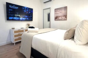 A hotel room with a bed, a TV mounted on the wall displaying various channels, a bedside table with a vase, and a framed picture on the wall. - Private 1 bedroom luxury mother-in-law suite close proximity to Midtown Tampa (Tampa)