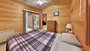 Una habitación con paneles de madera, una cama, un aparador y una puerta que da a un balcón.