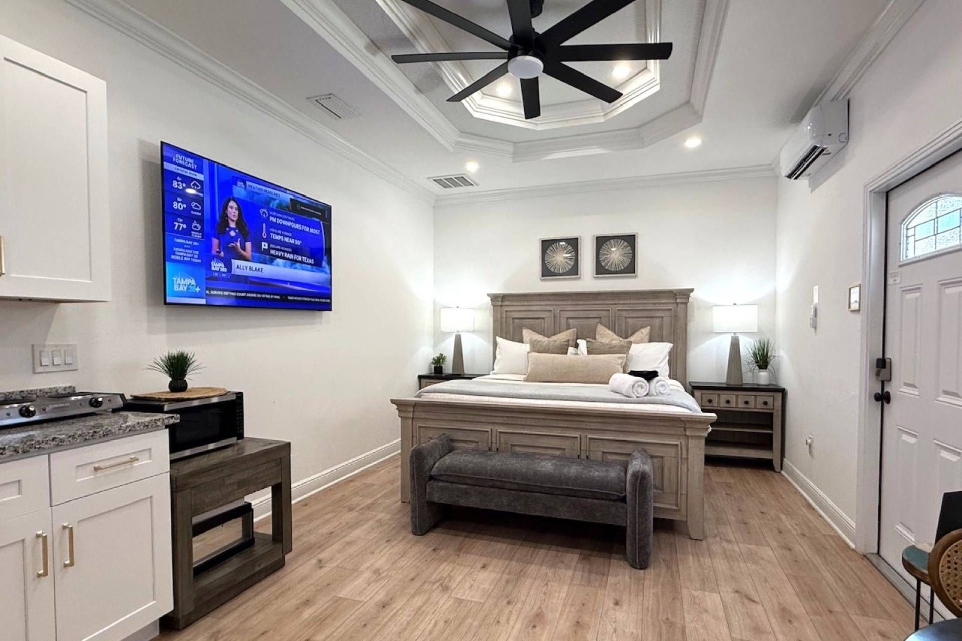 Una camera da letto con un letto, comodini, una ventola a soffitto e una televisione che mostra le previsioni del tempo.