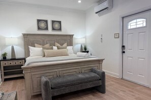 A bedroom with a bed, bedside tables, a bench, a door, and wall-mounted artwork.