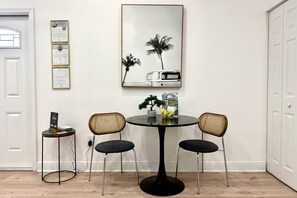 Uma área de refeições com uma mesa redonda, duas cadeiras, uma pequena mesa lateral com uma planta e certificados emoldurados na parede.