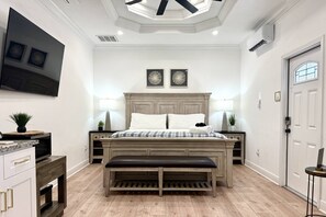 A bedroom with a bed, bench, wall-mounted TV, artwork, and a door.