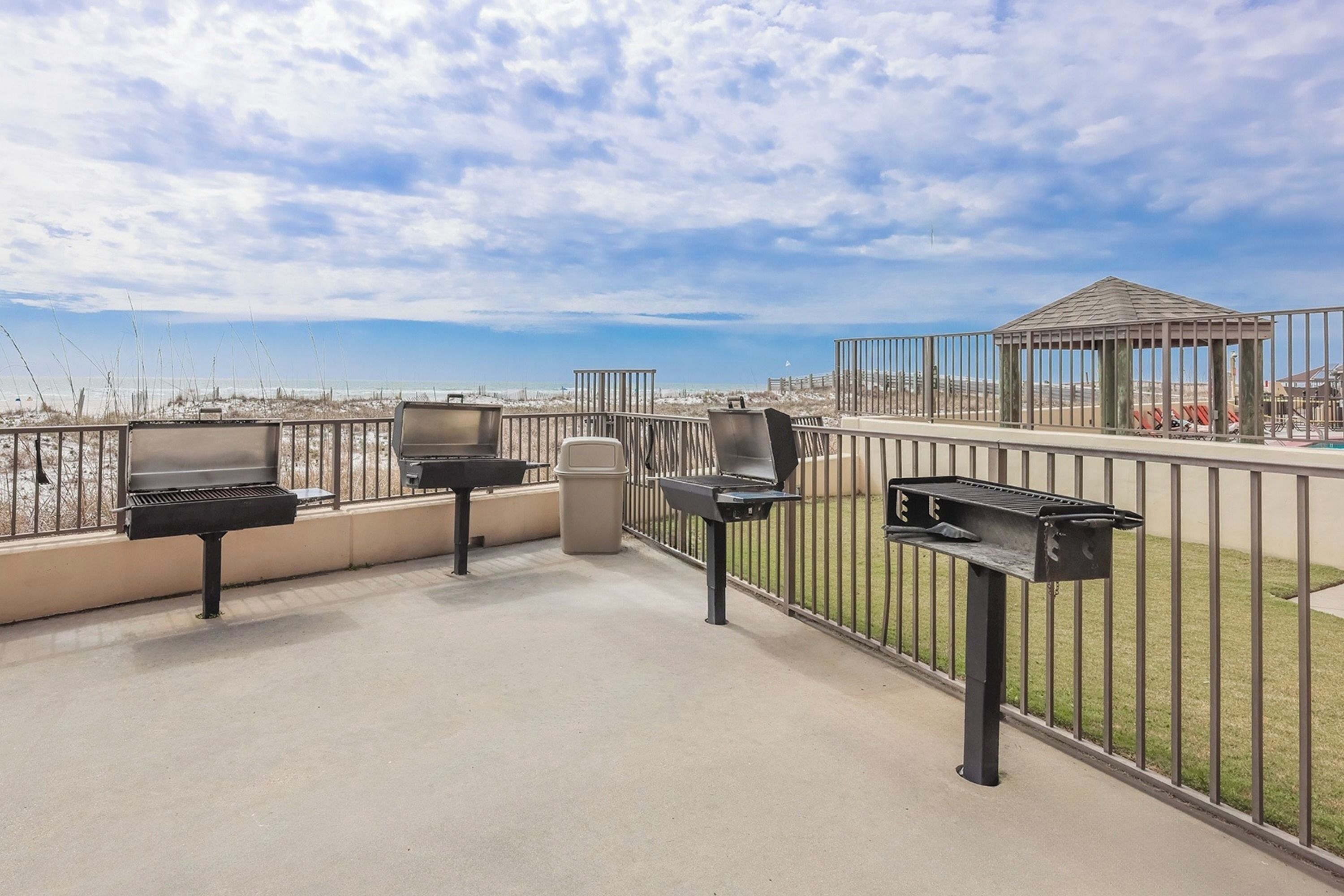 Um terraço no topo do prédio com churrasqueiras e uma lixeira, com vista para uma praia e um gazebo.