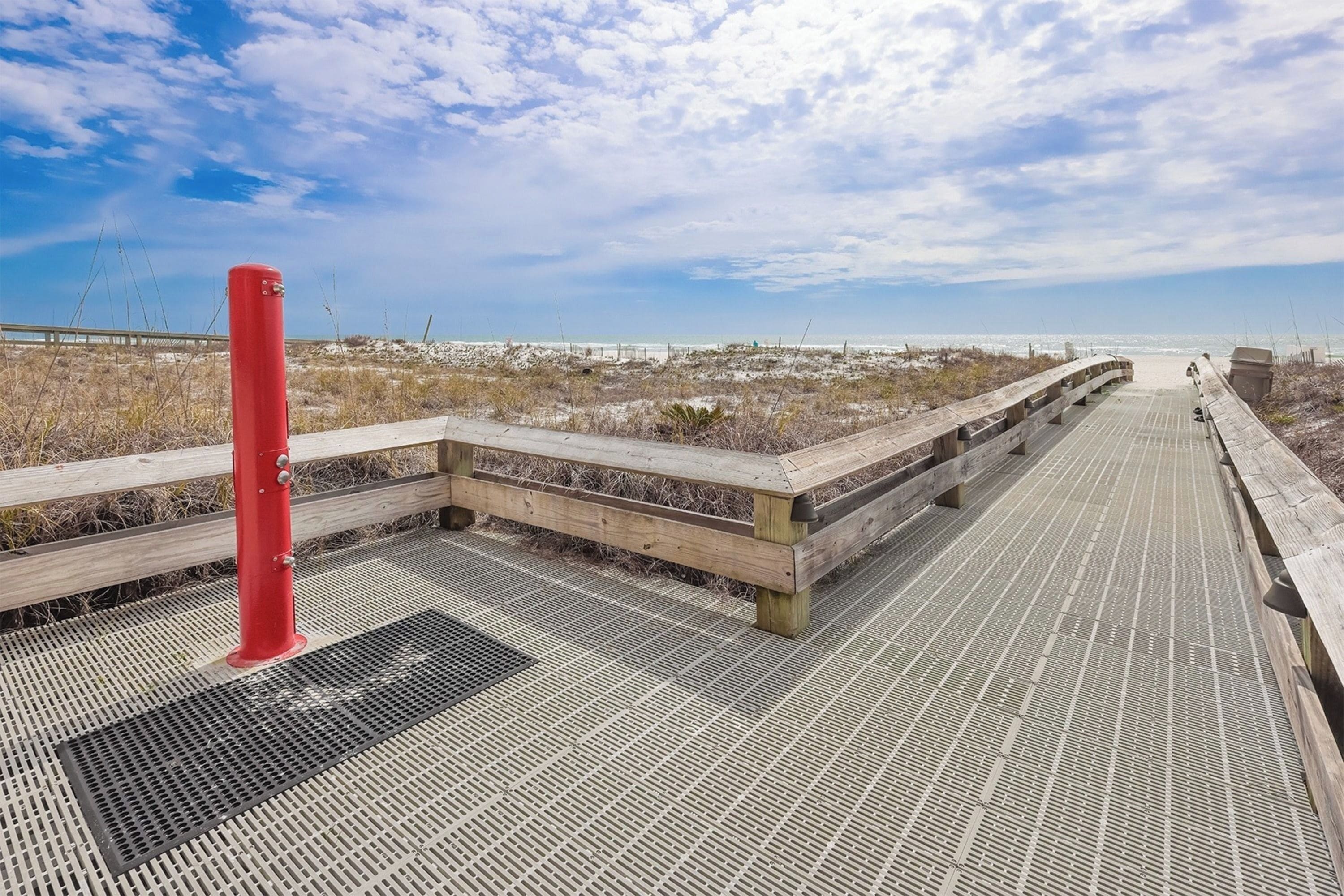 A wooden boardwalk leading to a beach with a red pole and a metal grate on the ground.