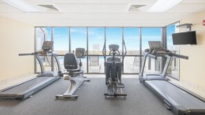 Ett gym med tre löpband, en crosstrainer och en motionscykel, med stora fönster som ger utsikt över staden.