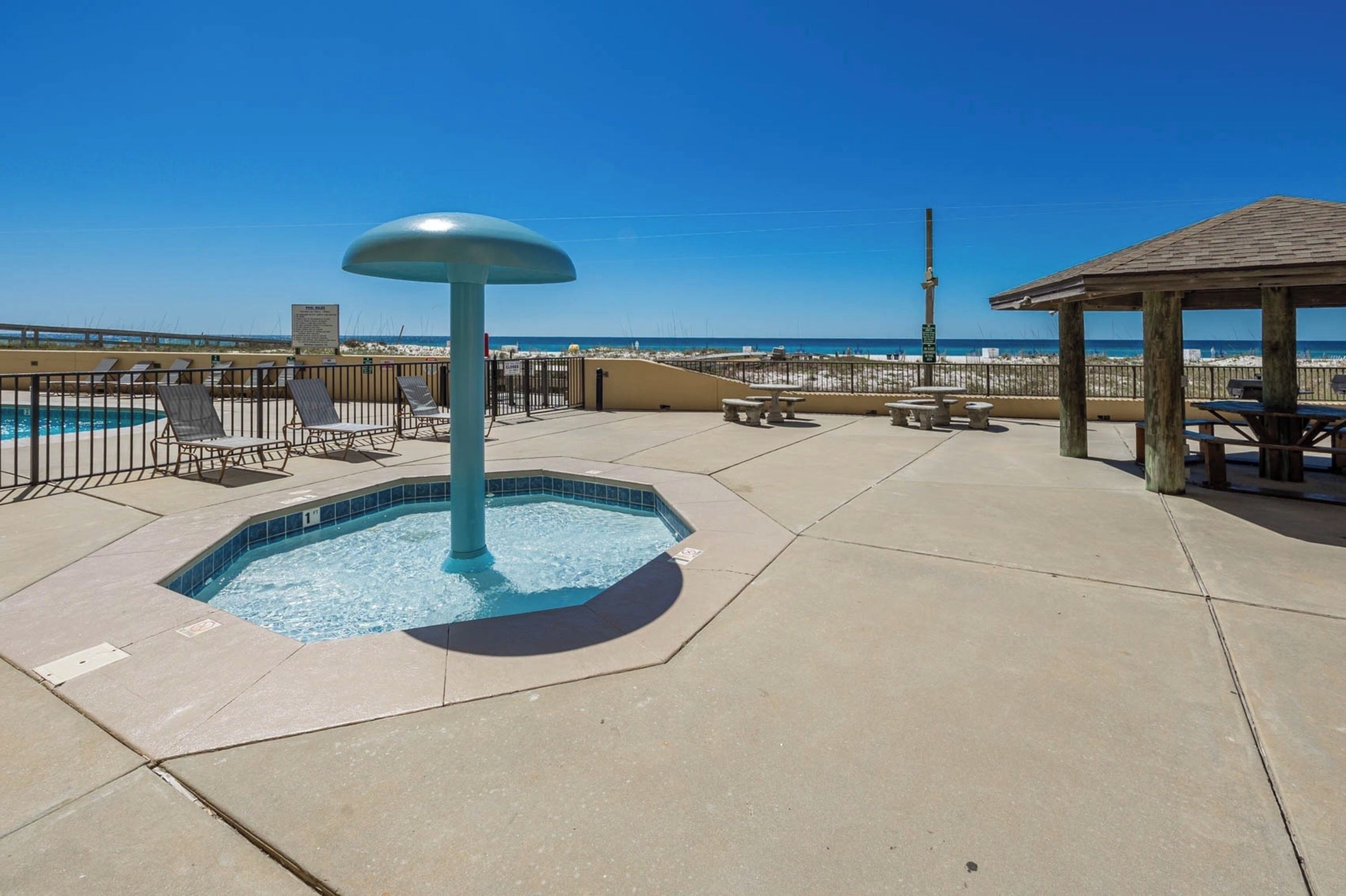 A pool area with a hot tub, lounge chairs, and a gazebo overlooking the beach.