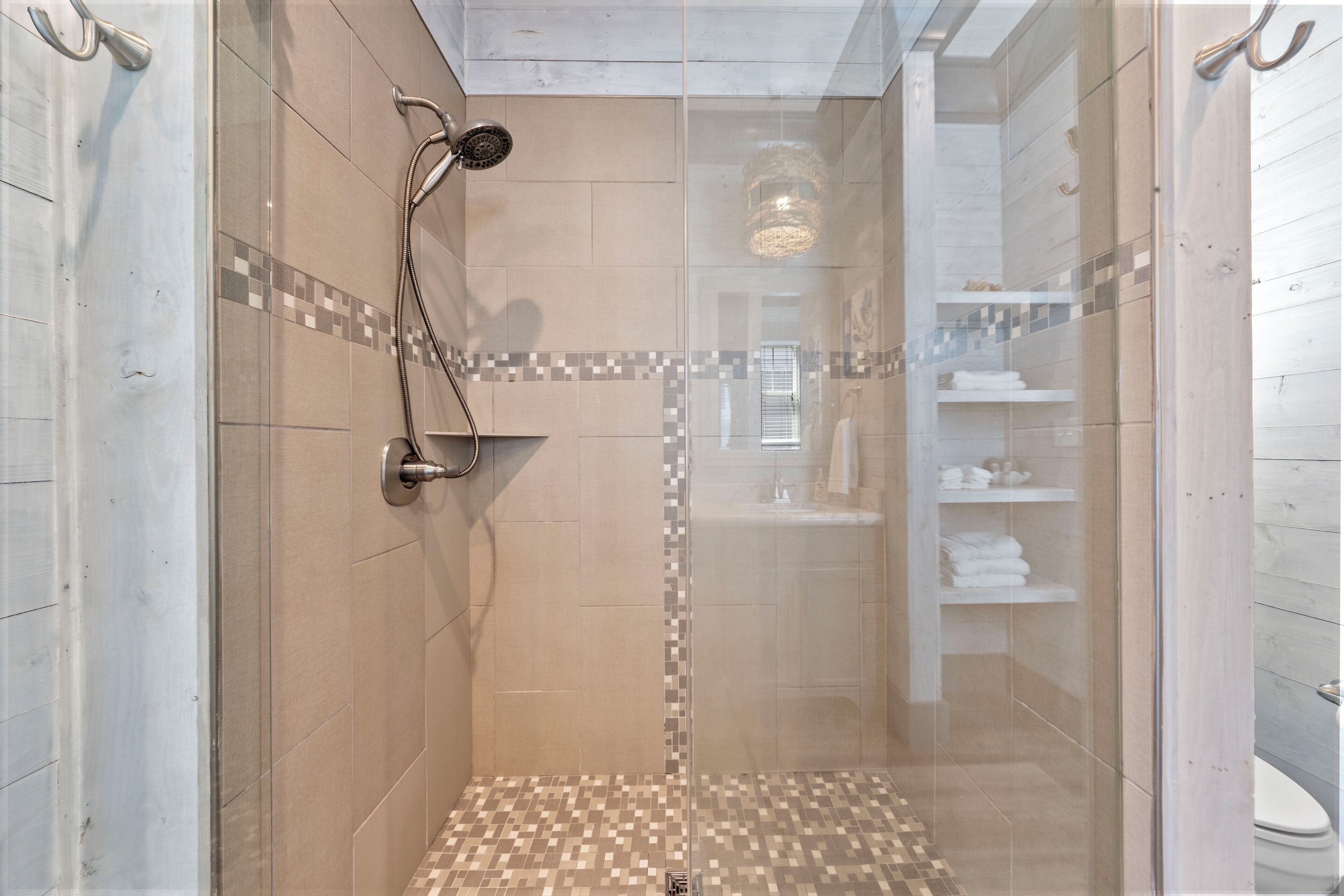 Une douche fermée par des parois en verre, avec un sol carrelé et un pommeau de douche.