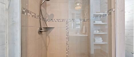 Une douche fermée par des parois en verre, avec un sol carrelé et un pommeau de douche.