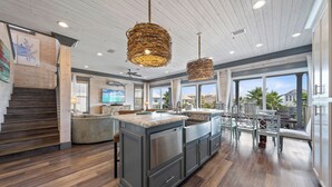 Une cuisine spacieuse dotée d’un grand îlot central, d’un plancher en bois foncé et offrant une vue sur l’extérieur.