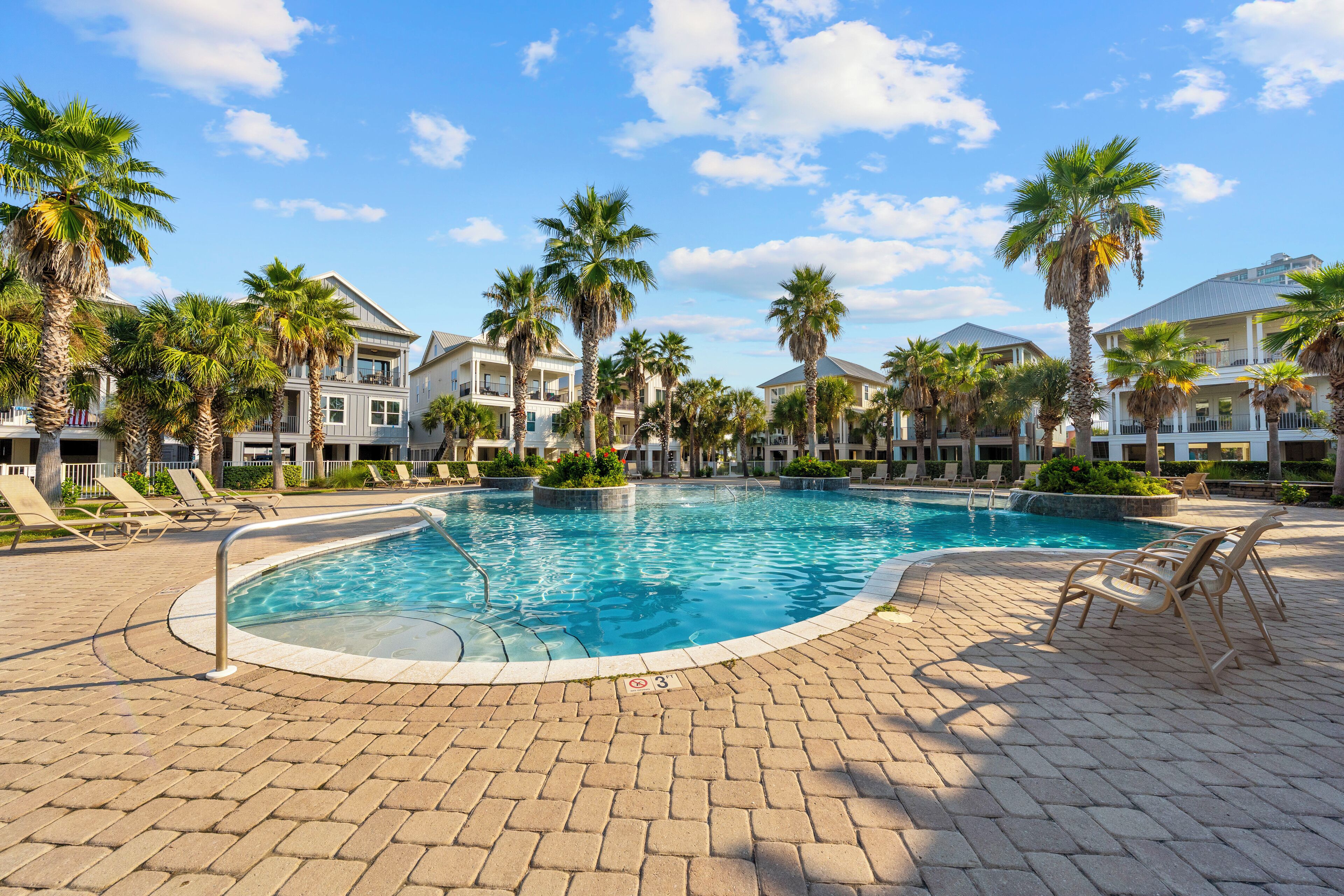 A swimming pool surrounded by palm trees and lounge chairs, with a brick pathway leading to it.